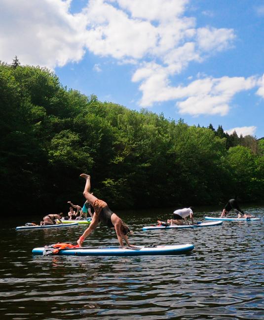 Picture of the yoga class on the water. A person in the tree position on the paddle-board